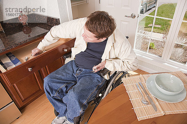 Mann mit Rückenmarksverletzung im Rollstuhl holt Geschirr aus dem Schrank  um den Tisch zu decken