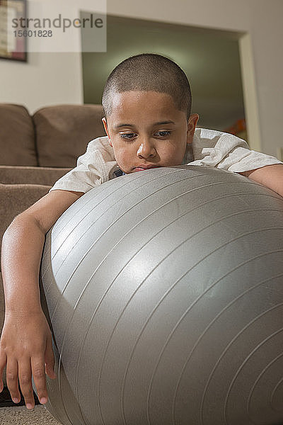 Hispanischer Junge mit Autismus spielt mit einem Gymnastikball im Wohnzimmer