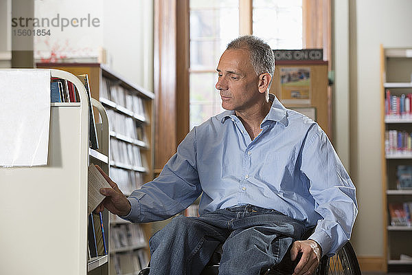 Mann im Rollstuhl mit einer Rückenmarksverletzung ordnet Bücher in einer Bibliothek