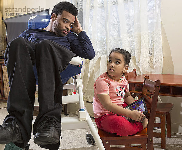 Afroamerikanischer Mann mit zerebraler Lähmung und seiner Tochter  die zu Hause ein Tablet benutzt