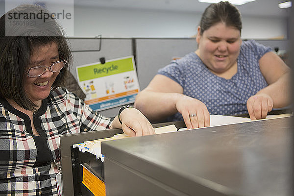 Zwei Frauen mit Lernschwierigkeiten benutzen einen Aktenschrank in einem Büro