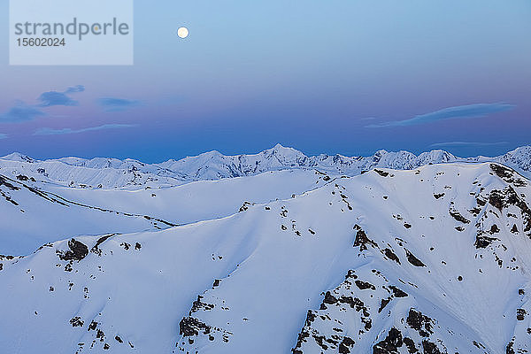 Der Mond geht nach Sonnenuntergang über schneebedeckten Bergkämmen in der Alaska Range auf; Alaska  Vereinigte Staaten von Amerika