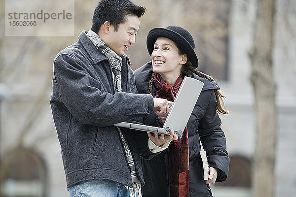 Seitenprofil eines jungen Mannes  der einen Laptop benutzt  und einer jungen Frau  die ihn ansieht