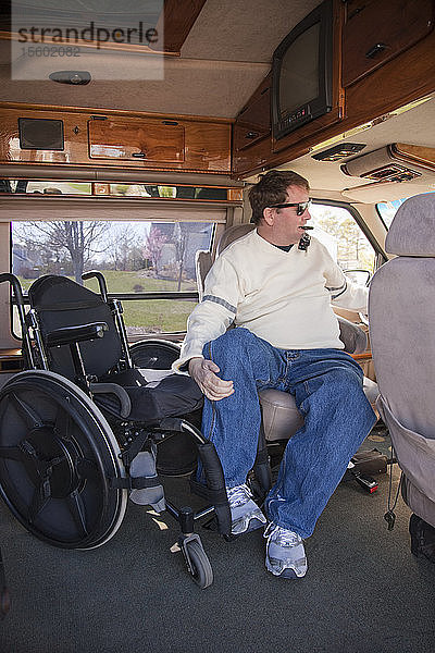 Mann mit Querschnittslähmung steigt aus seinem Rollstuhl in den Fahrersitz eines behindertengerechten Transporters