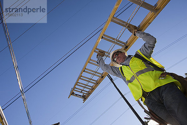 Ingenieur  der eine Leiter trägt  um Geräte an Strommasten zu installieren