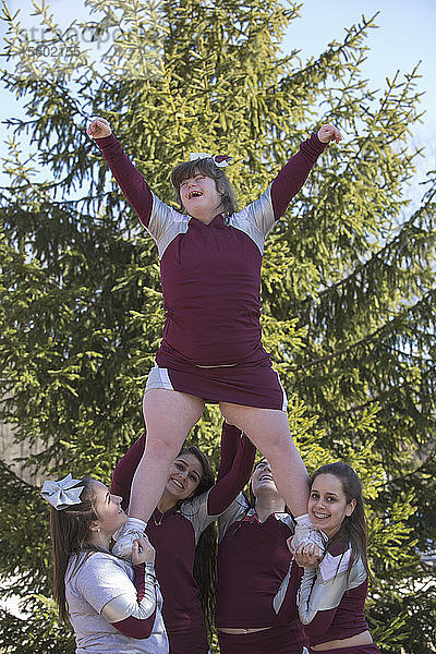 Cheerleader heben einen Cheerleader mit Down-Syndrom in die Luft