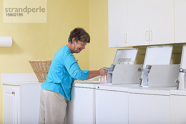 Ältere Frau legt Wäsche in eine Waschmaschine