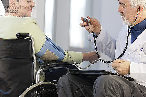 Arzt mit Muskeldystrophie im Rollstuhl prüft den Blutdruck eines Patienten