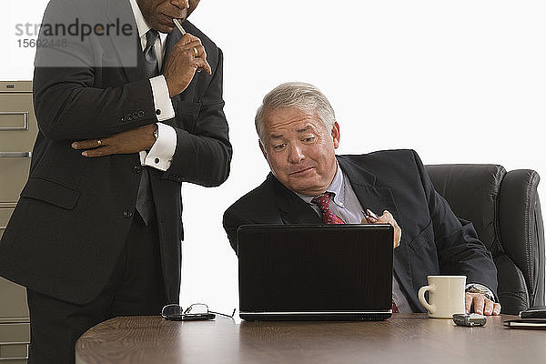 Geschäftsmann  der auf einen Laptop schaut  während ein anderer Geschäftsmann neben ihm steht