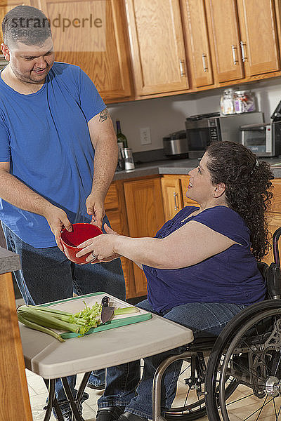 Frau mit Spina Bifida und ihr Mann bereiten das Abendessen in ihrer Küche vor