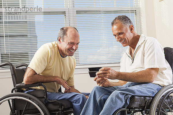 Zwei behinderte Männer sitzen in Rollstühlen und benutzen ein Smartphone