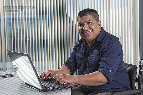 Hispanischer Mann mit Rückenmarksverletzung arbeitet in einem Büro