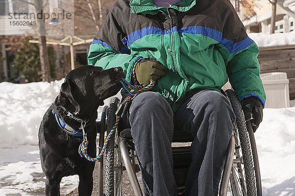 Frau mit Multipler Sklerose in einem Rollstuhl mit einem Diensthund im Schnee
