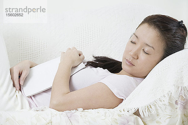 Seitenprofil einer jungen Frau  die ein Buch hält und auf einer Couch schläft