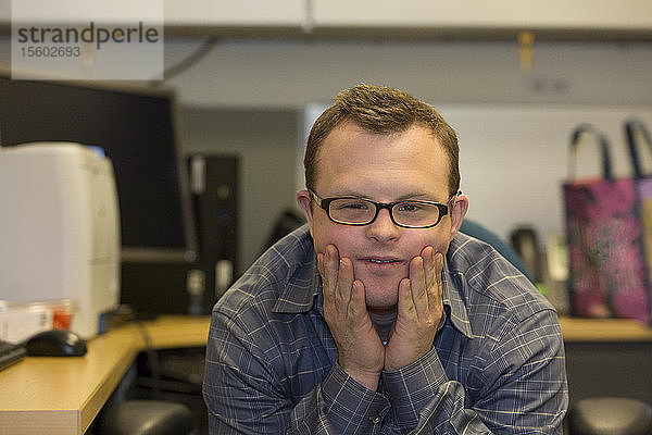 Porträt eines Krankenhausmitarbeiters mit Down-Syndrom  der an seinem Schreibtisch sitzt