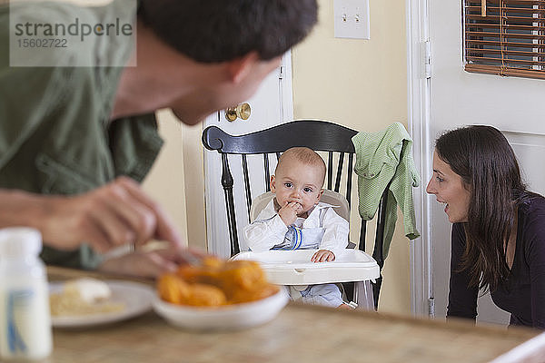 Vater bereitet die Mahlzeit für das Baby zu und die Mutter schaut zu