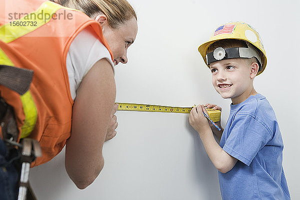 Blick auf eine Frau und einen Jungen  die eine Wand mit einem Maßband messen.