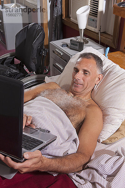 Mann mit Querschnittslähmung im Bett mit seinem Laptop