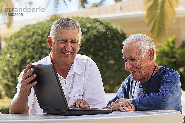 Älterer  sehbehinderter Mann  der mit seinem Sohn einen Laptop benutzt