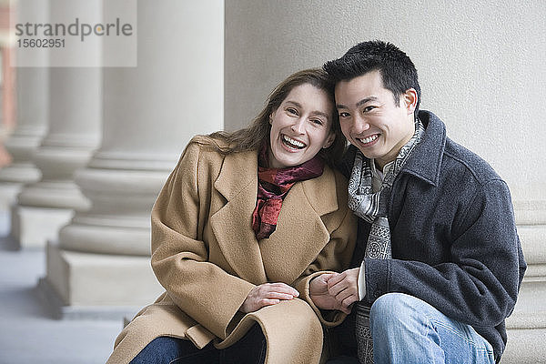 Porträt eines jungen Paares  das vor einer Säule sitzt und lächelt