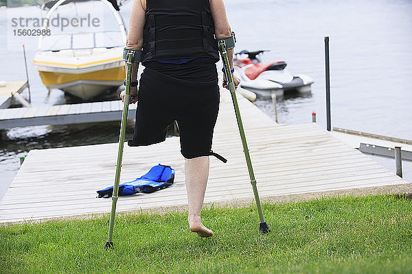 Frau mit Beinprothese und Krücken auf dem Weg zum Wasserskifahren