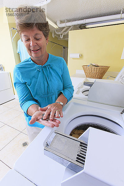 Ältere Frau zählt das Wechselgeld für eine gewerbliche Waschmaschine in einer Waschküche