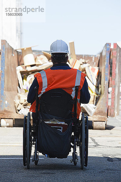 Gebäudetechniker im Rollstuhl mit Rückenmarksverletzung nähert sich einem Müllcontainer