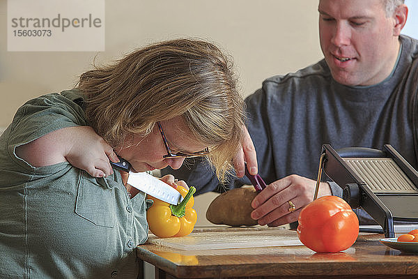 Frau mit TAR-Syndrom schneidet zusammen mit ihrem Mann in der Küche Gemüse