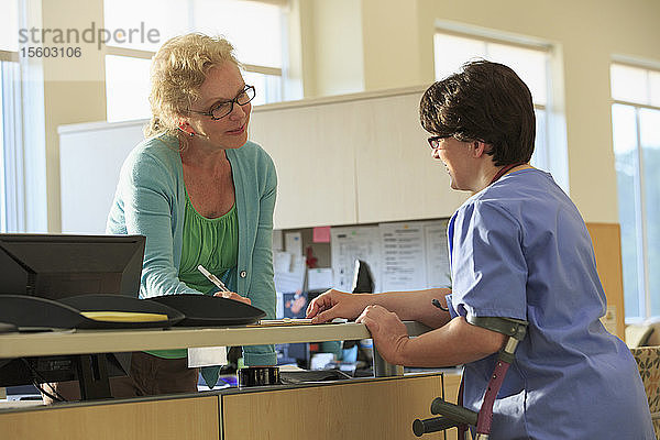 Krankenschwester mit Cerebralparese fragt bei der Verwaltung nach den Unterlagen eines Patienten in einer Klinik