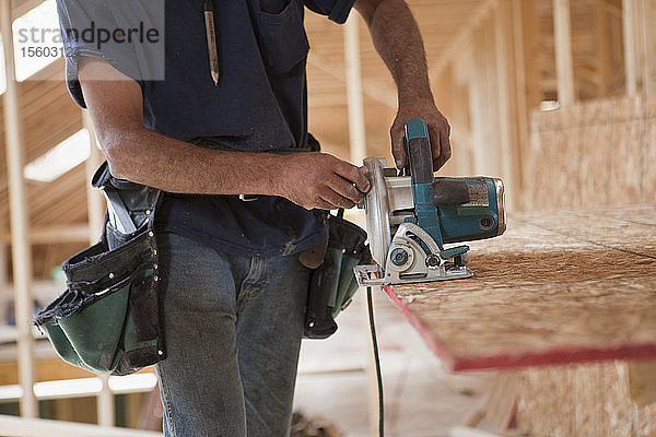 Spanischer Zimmermann bei der Arbeit mit einer Kreissäge an einer Dachplatte in einem im Bau befindlichen Haus