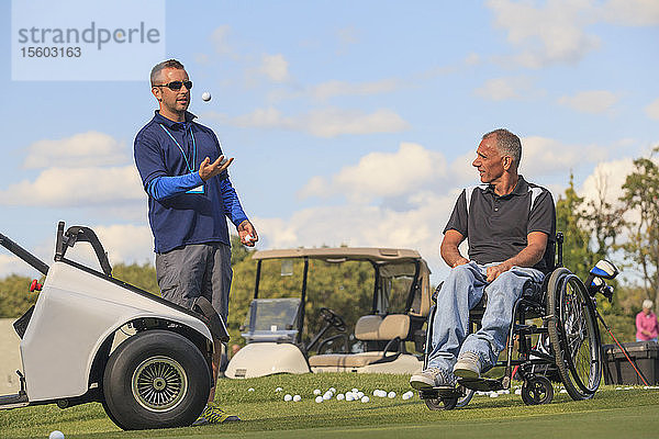 Mann mit Rückenmarksverletzung in einem adaptiven Wagen  der zusammen mit seinem Assistenten Golf spielen soll