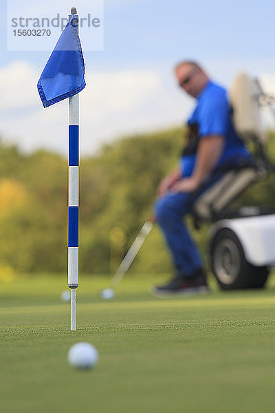 Mann mit Rückenmarksverletzung in einem adaptiven Wagen auf dem Golf-Putting-Green