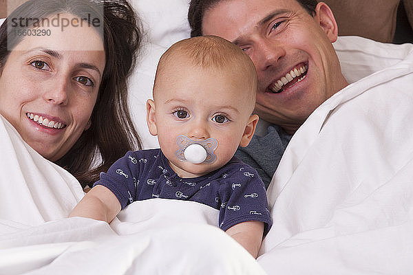 Eltern im Bett mit ihrem Sohn  der einen Schnuller trägt