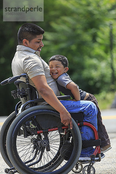 Glücklicher spanischer Mann mit Rückenmarksverletzung im Rollstuhl mit seinem Sohn