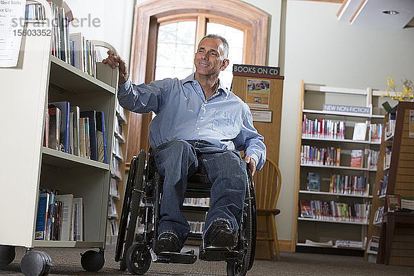 Mann im Rollstuhl mit einer Rückenmarksverletzung verschiebt ein Bücherregal in einer Bibliothek