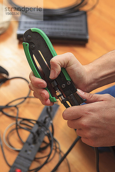 Kabelinstallateur  der mit einer Crimpzange einen neuen Kabelstecker an ein Kabel anbringt