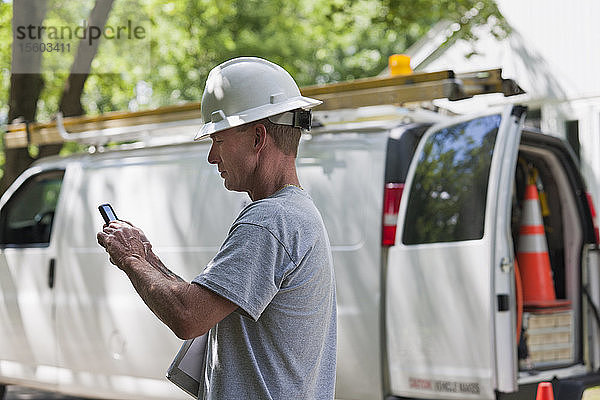 Kabelinstallateur prüft Arbeitsauftrag für Installation auf Smartphone