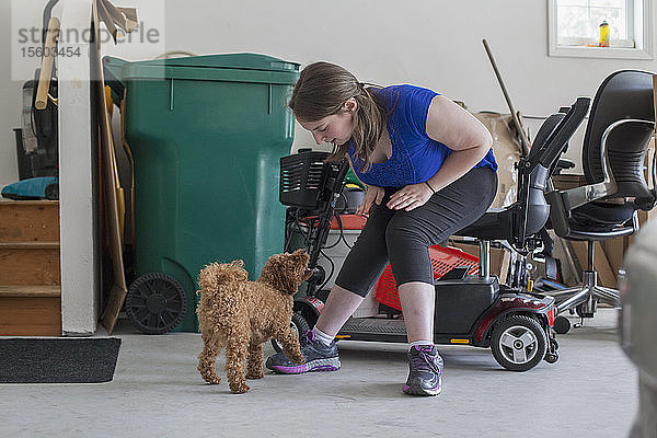 Junge Frau mit zerebraler Lähmung spielt mit ihrem Hund  während ihr Roller da ist