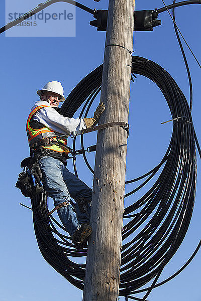 Kabelmonteur auf einem Strommast beim Verlegen eines neuen Kabels