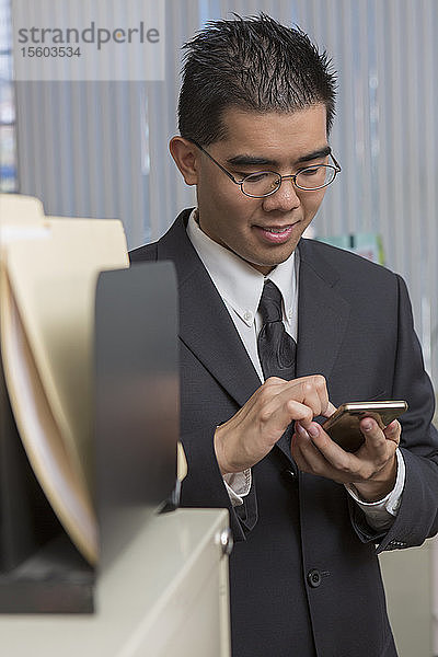 Glücklicher asiatischer Mann mit Autismus benutzt sein Telefon in einem Büro