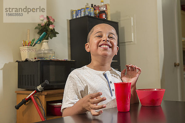 Glücklicher hispanischer Junge mit Autismus beim Essen in seiner Küche