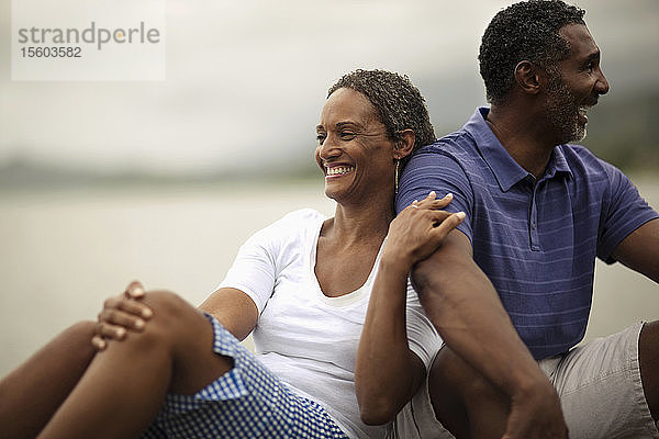 Glückliches Paar im mittleren Erwachsenenalter  das zusammen am Rande einer Uferpromenade sitzt