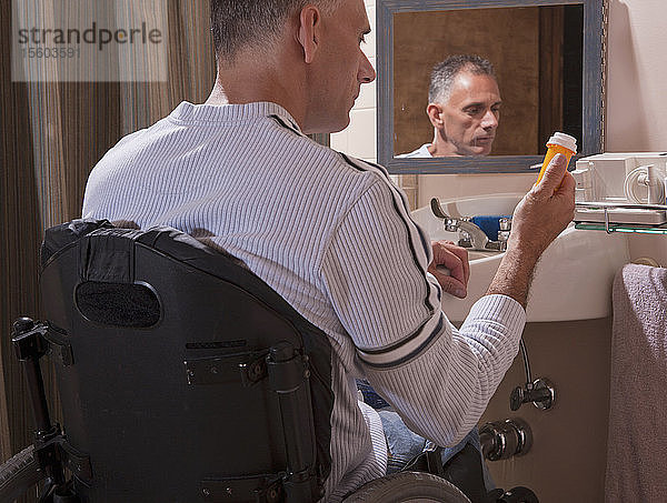 Mann mit Rückenmarksverletzung im Rollstuhl schaut auf eine Pillenflasche
