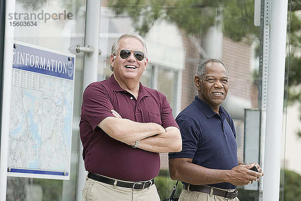 Zwei Geschäftsleute stehen an einer Bushaltestelle und lächeln