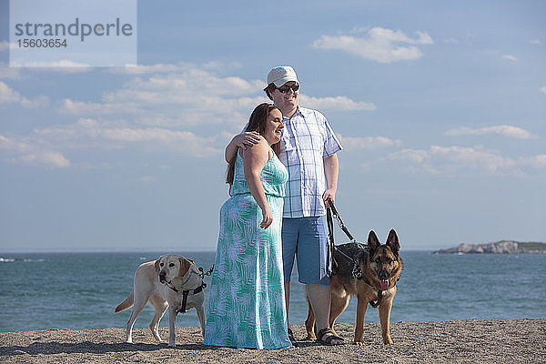 Junges Paar mit Sehbehinderung und Diensthunden am Strand
