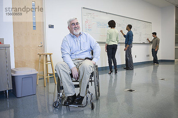 Universitätsprofessor mit Muskeldystrophie in einem Rollstuhl mit seinen Studenten im Hintergrund