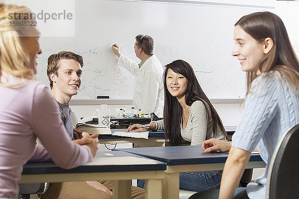 Studenten unterhalten sich in einer Ingenieursklasse  während der Professor an der Tafel schreibt