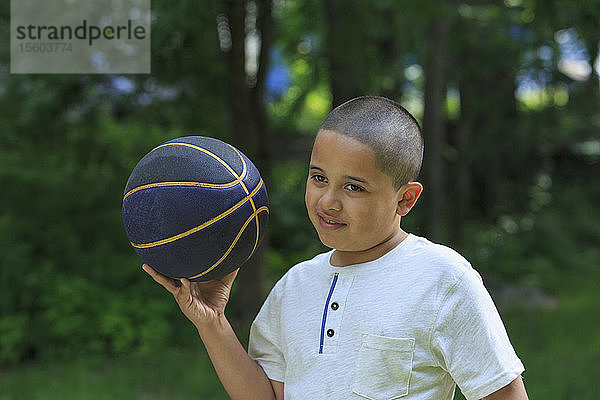 Hispanischer Junge mit Autismus spielt mit einem Basketball im Park