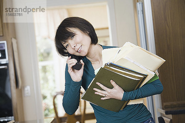 Porträt einer erwachsenen Frau  die einen Stapel Akten hält und mit einem Mobiltelefon spricht