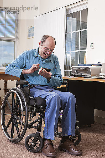 Mann mit Friedreich-Ataxie im Rollstuhl benutzt ein Smartphone mit deformierten Händen